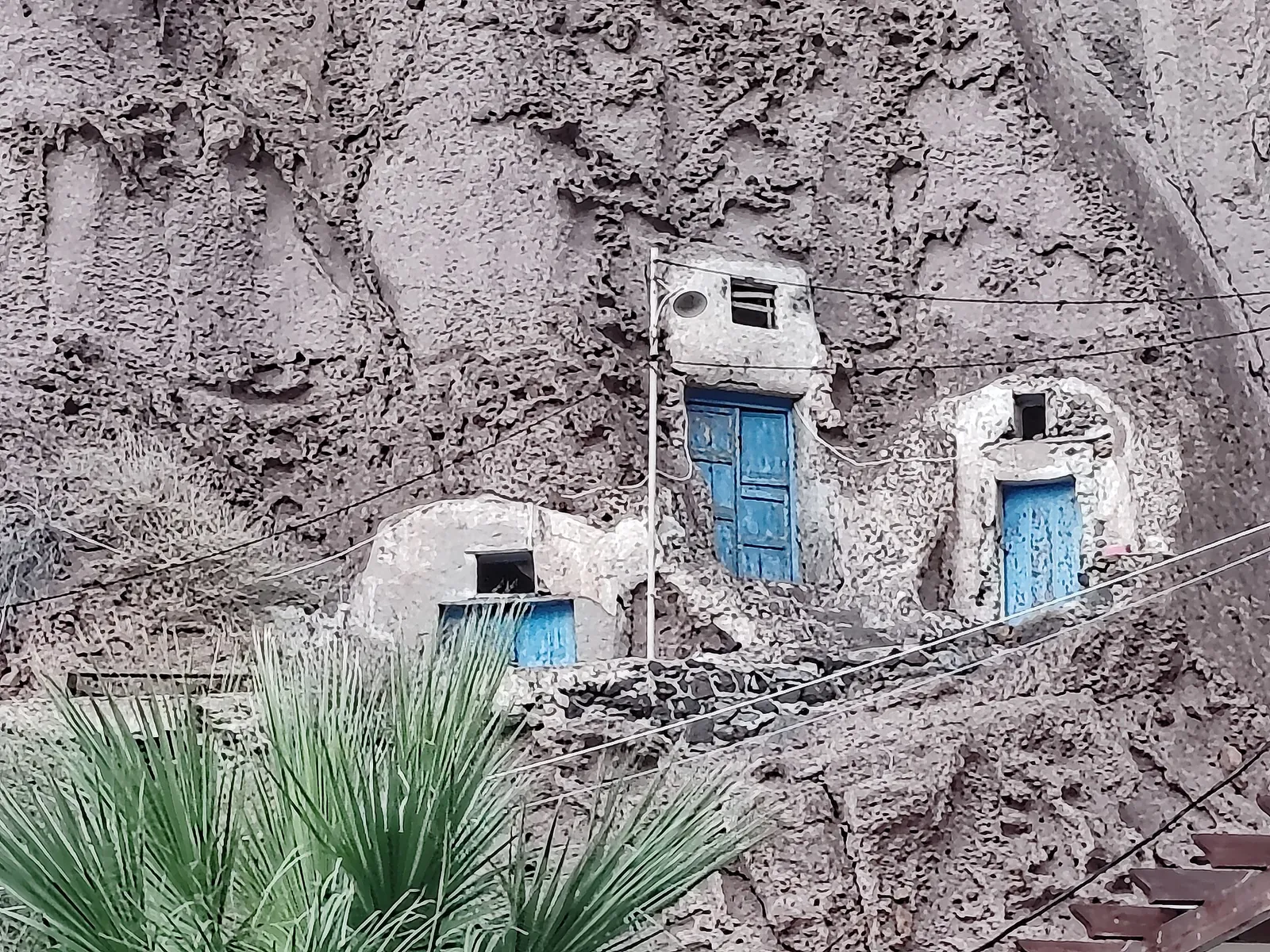 Three small cave dwellings dug into the volcanic rock, with blue wooden doors