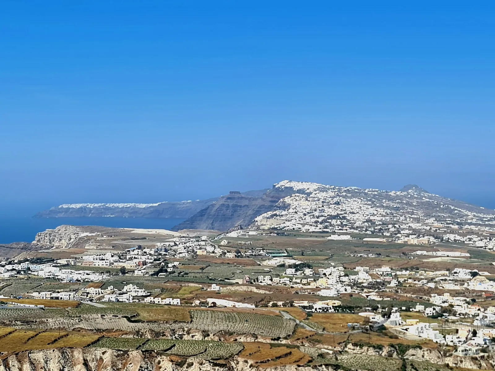 Vineyards and villages on the plain below Pyrgos, with Fira and Oia along the caldera ridge