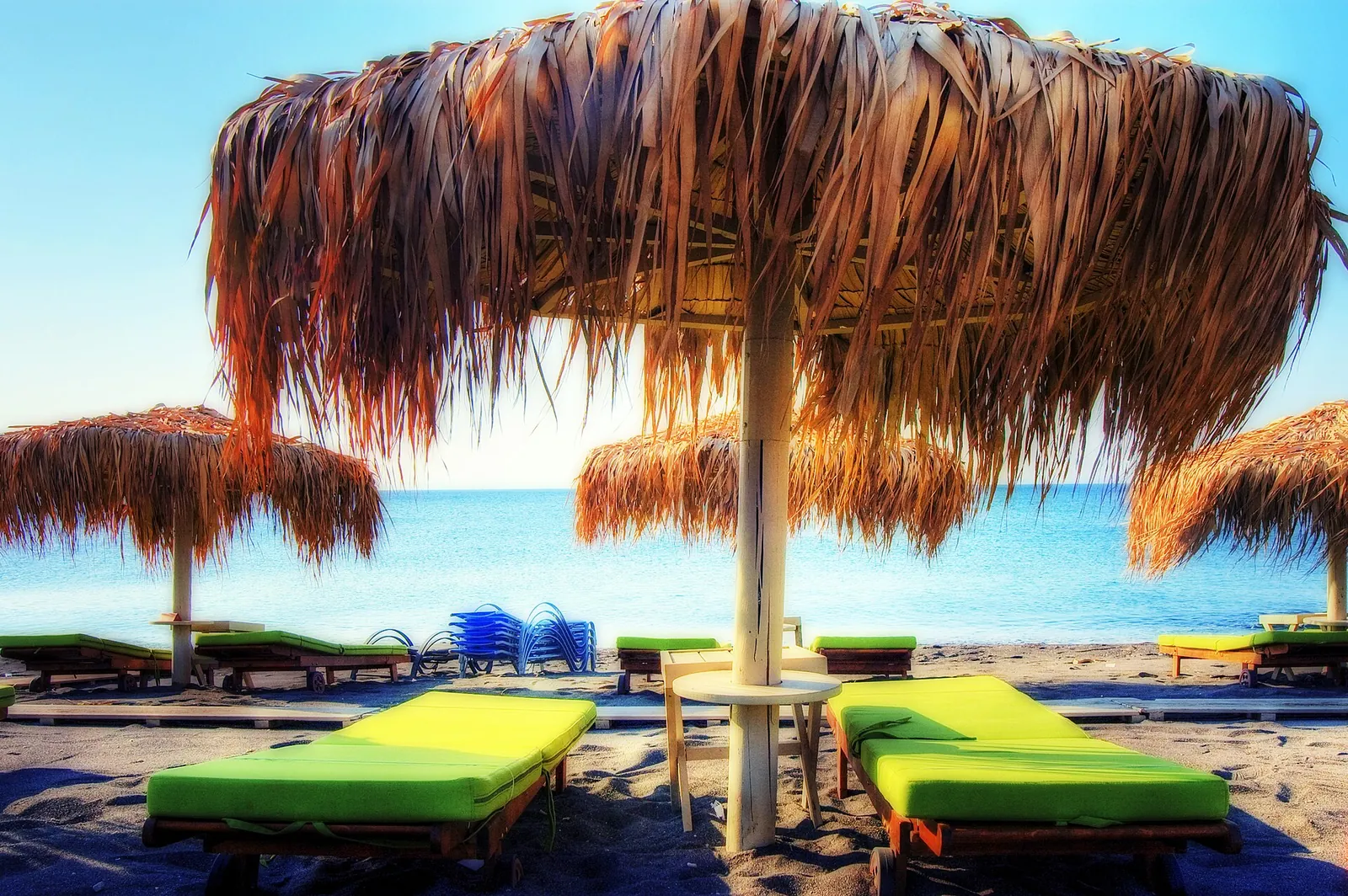 Straw umbrellas over green sunbeds on Perivolos beach