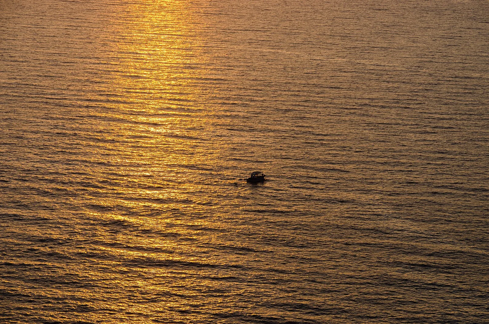 Gold evening light on the sea off Cape Akrotiri, a small boat crossing it