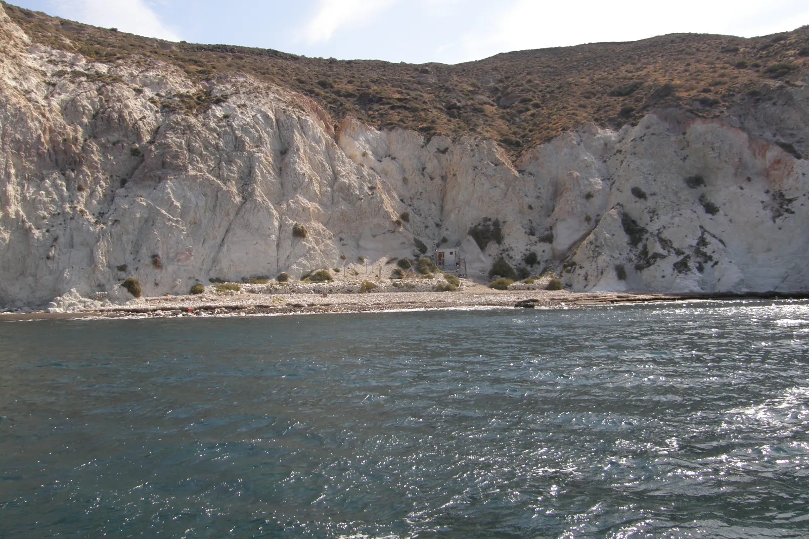 White Beach (Aspri Paralia) in Santorini seen from the sea, tall white cliffs above a narrow pebble beach