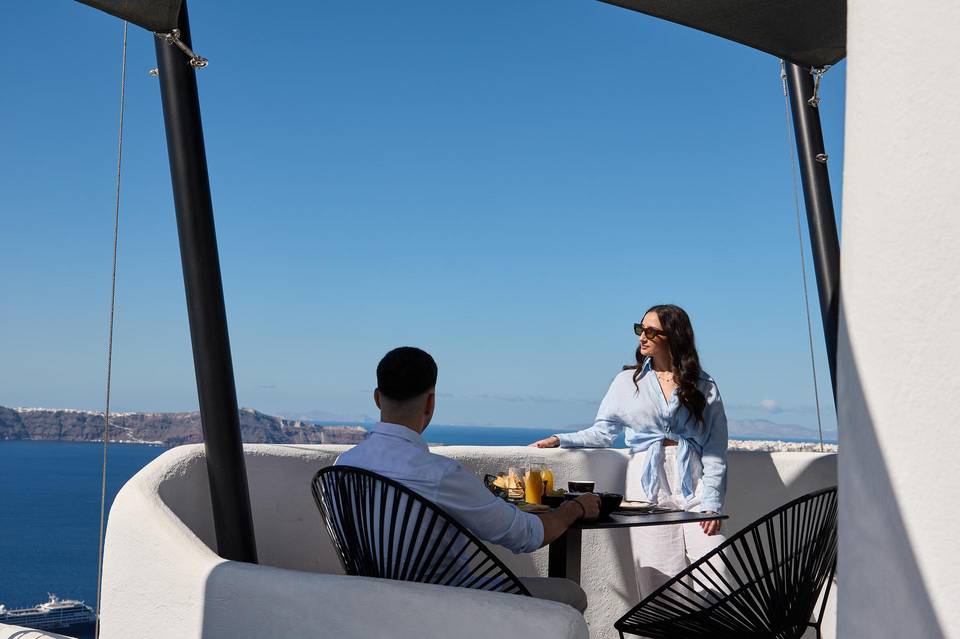 Couple enjoying breakfast on a rooftop terrace with Santorini caldera views at Aroma Suites